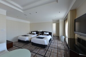 Habitación de hotel con dos camas, televisión, escritorio y alfombra estampada.