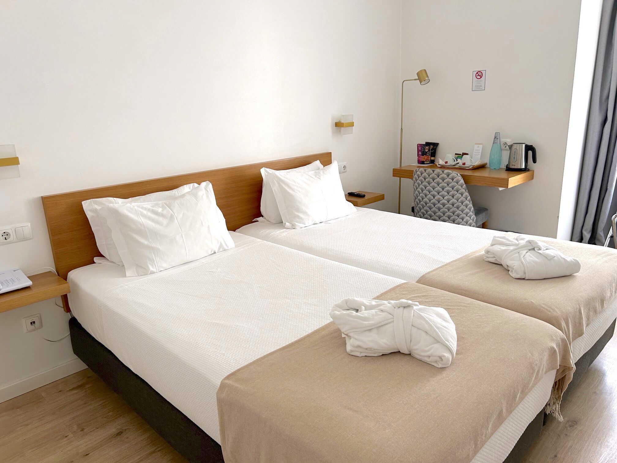 Une chambre d’hôtel avec deux lits, un bureau avec une lampe, une chaise et une petite étagère avec quelques objets.