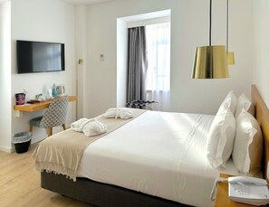 Une chambre d’hôtel équipée d’un lit, d’un bureau, d’une chaise, d’une télévision, d’un téléphone et d’une fenêtre avec des rideaux.