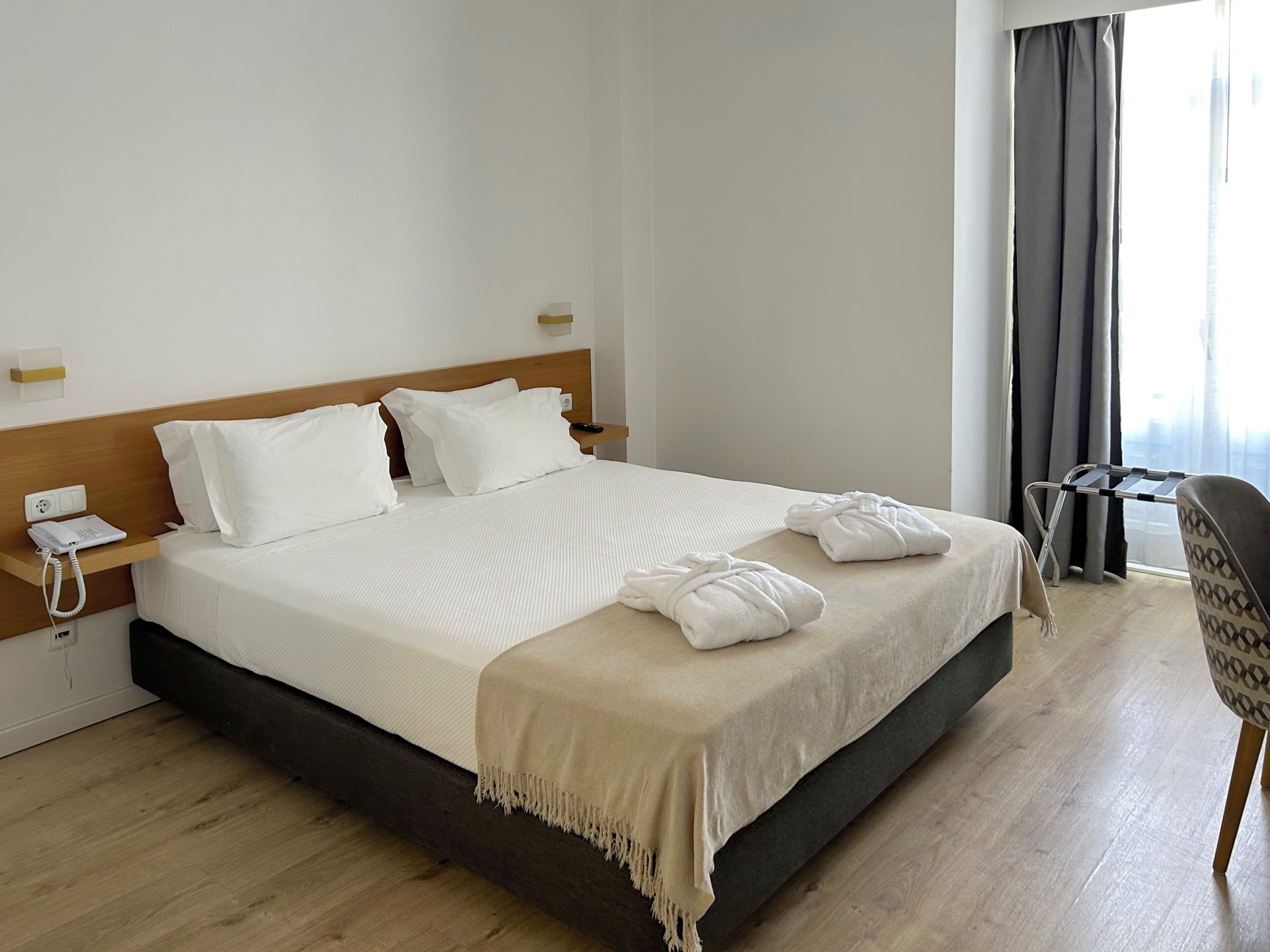 Une chambre d’hôtel avec un grand lit, une table de chevet avec un téléphone, une chaise et une fenêtre avec des rideaux.