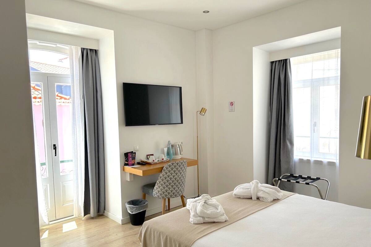 Habitación de hotel con cama, escritorio con televisor de pantalla plana, una silla, lámpara de pie y ventana con cortinas.