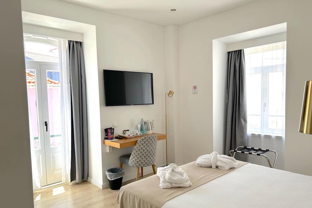 Habitación de hotel con cama, escritorio con televisor de pantalla plana, una silla, lámpara de pie y ventana con cortinas.