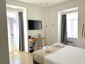 Habitación de hotel con cama, escritorio con televisor de pantalla plana, una silla, lámpara de pie y ventana con cortinas.