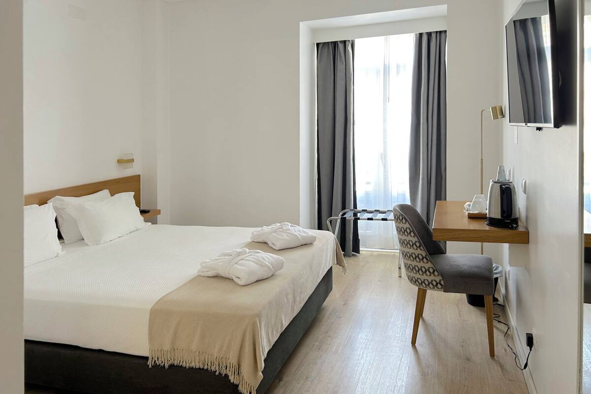 Una habitación de hotel con cama, escritorio, silla, televisión y ventana con cortinas.