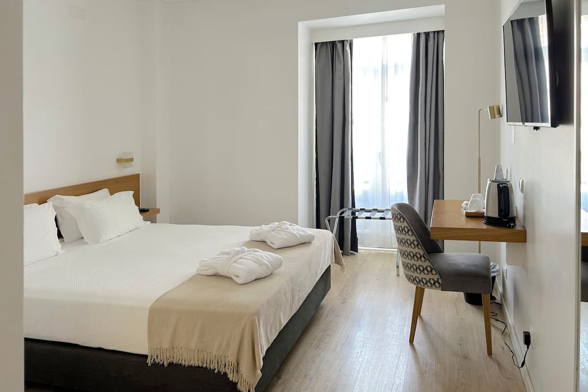 Una habitación de hotel con cama, escritorio, silla, televisión y ventana con cortinas.
