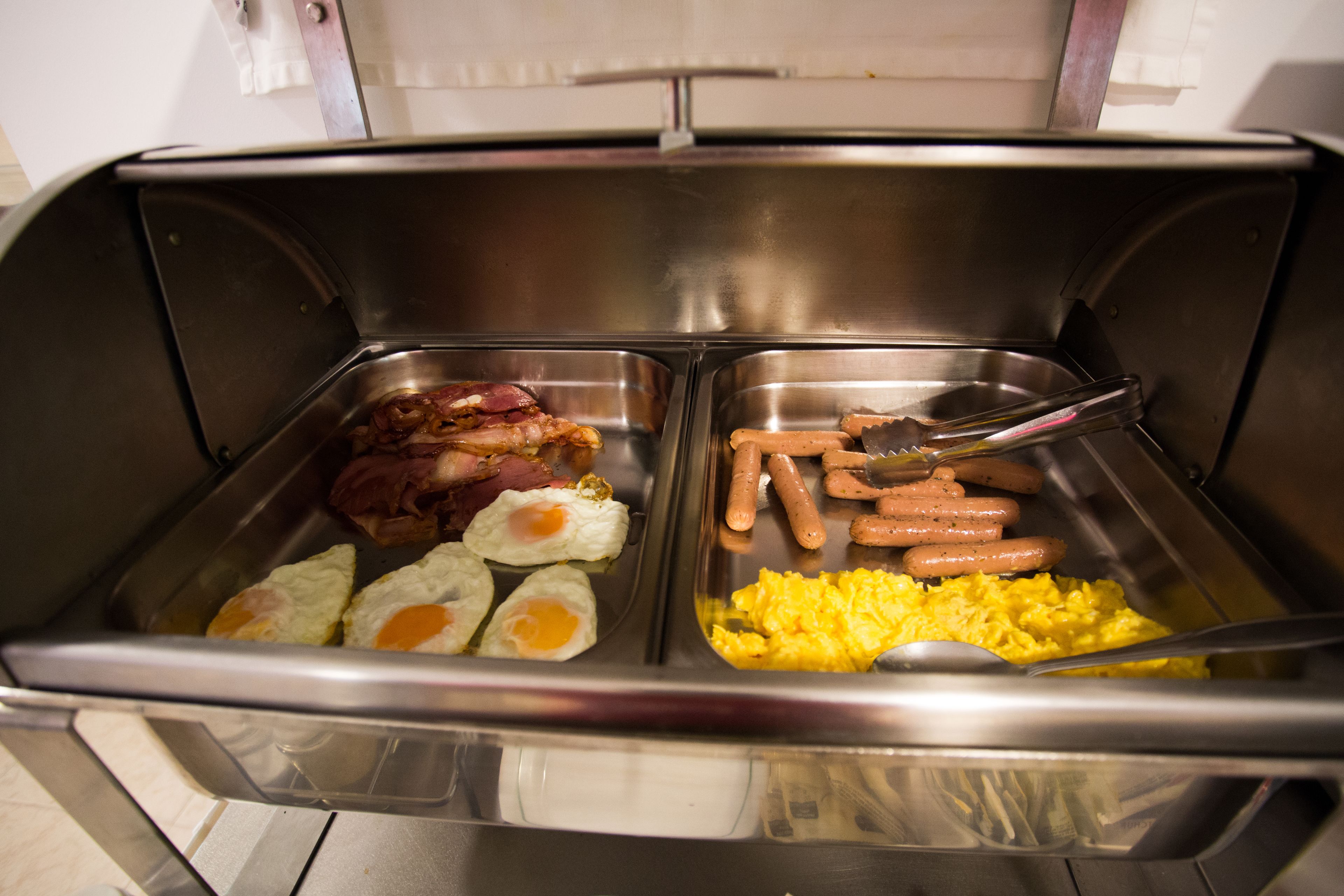Un bufé con diversas opciones de desayuno, como tocino, salchichas, huevos y huevos revueltos.