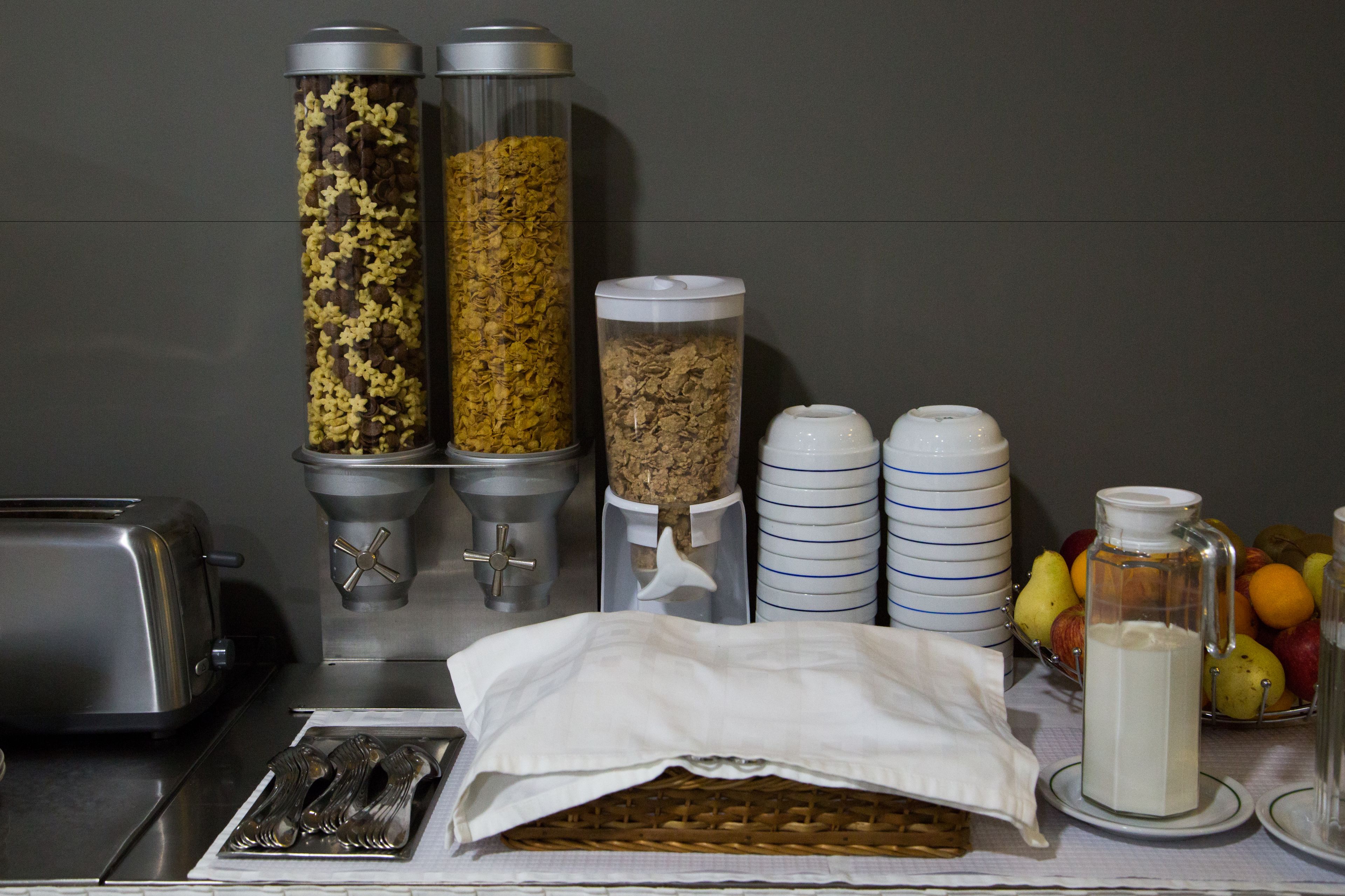 A breakfast bar with food dispensers, a toaster, and a fruit basket.