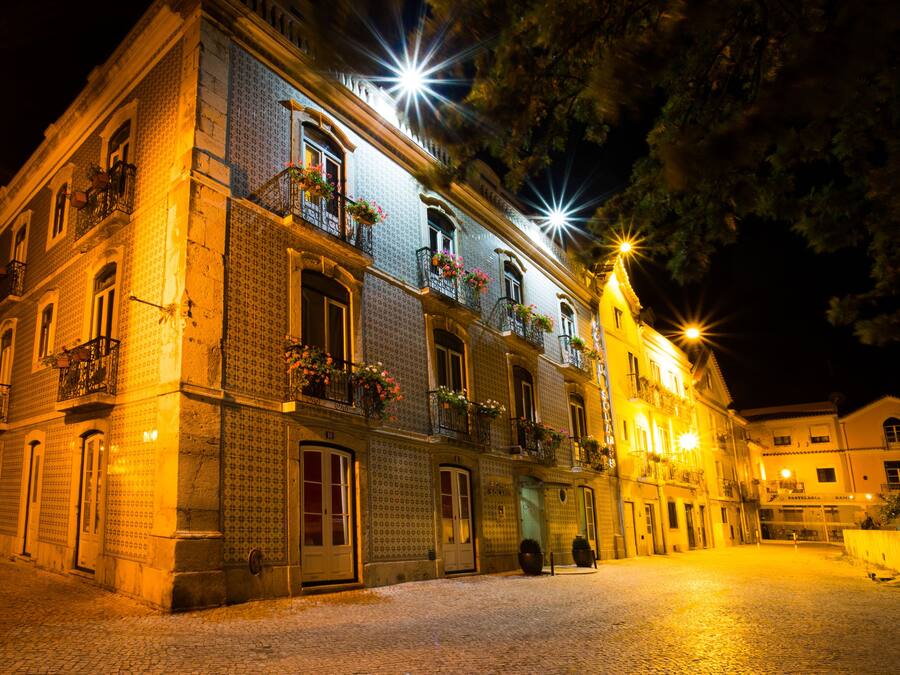 A historic building with multiple balconies, large windows, and a cobblestone street at night.