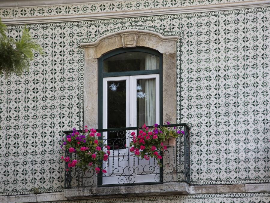 Fachada de edificio con diseño de baldosas estampadas, ventana con arco decorativo y balcón con jardineras.
