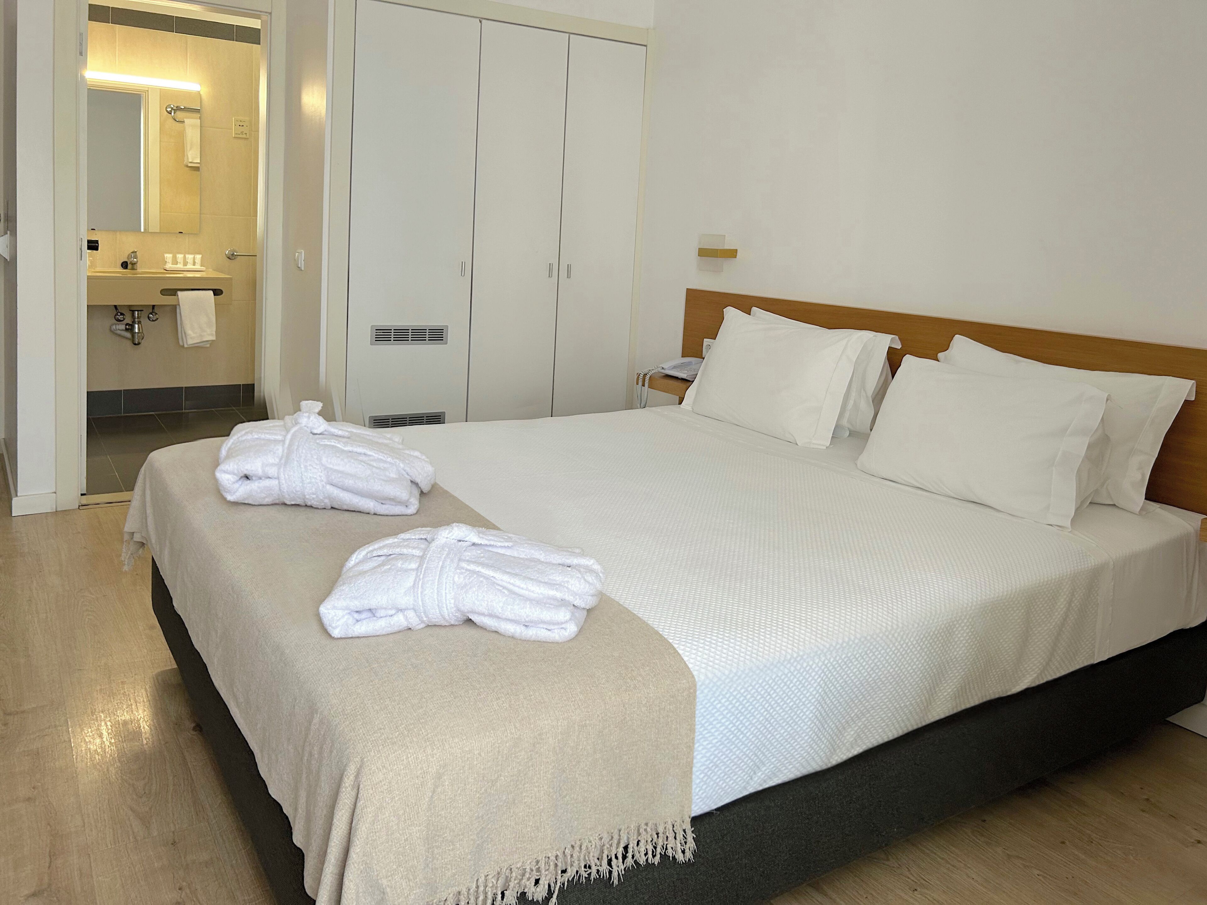 A hotel room with a bed, a bathroom with a mirror, and a wardrobe.