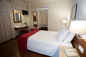 Comfortable room with a neatly made bed, desk, chair, telephone, and mirror.