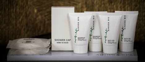 Et sæt AINHOA BIO produkter, herunder en badehætte, shampoo og badesæbe, alt sammen med hvid emballage og grønne bladmotiver.
