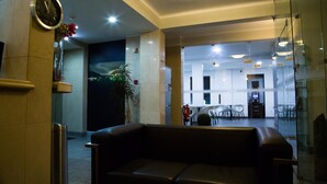 A lobby with a leather sofa, a clock, a fire extinguisher, and a bar area in the background. - Hotel Solaris (Setubal)