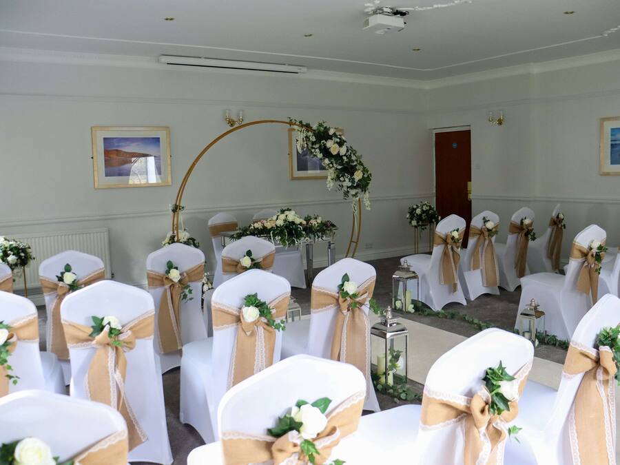 A wedding ceremony setup with rows of chairs, floral decorations, and a wooden arch.