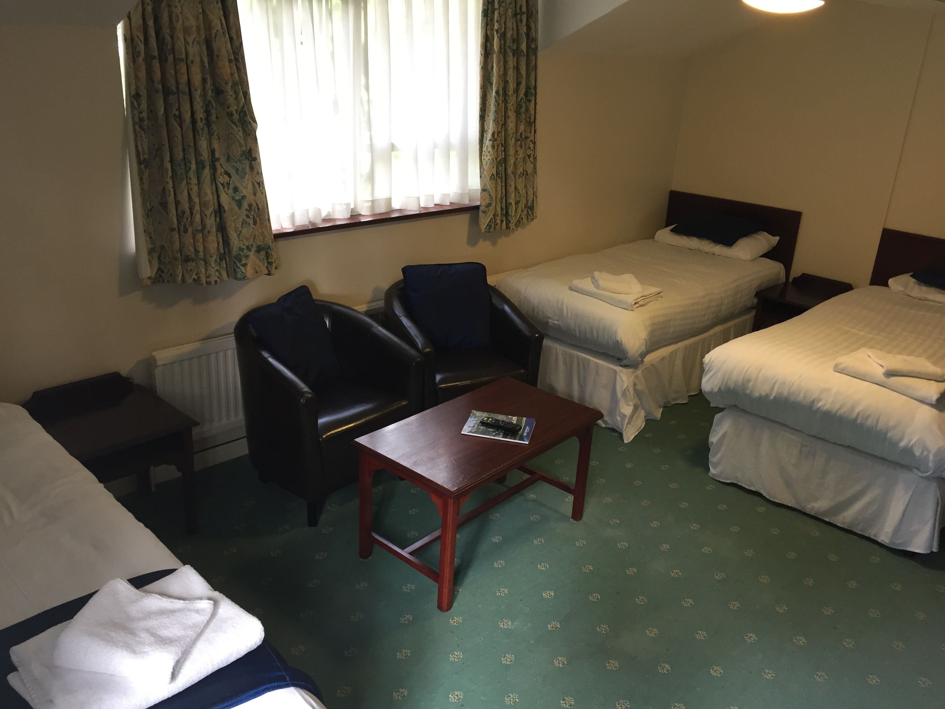 A hotel room with two single beds, a desk, a chair, and a window with curtains.
