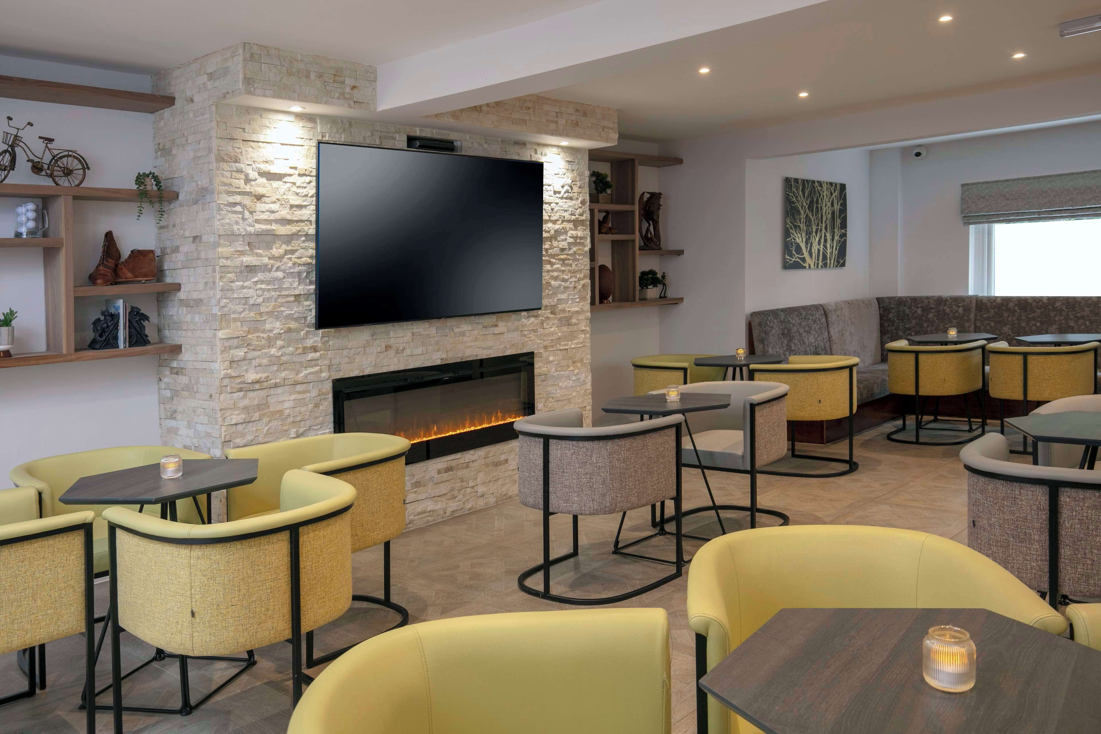 A modern lounge area with a stone wall, flat-screen TV, seating, and a fireplace.