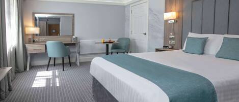 Een hotelkamer met een groot bed, een bureau met stoel, een kleine tafel en een spiegel.