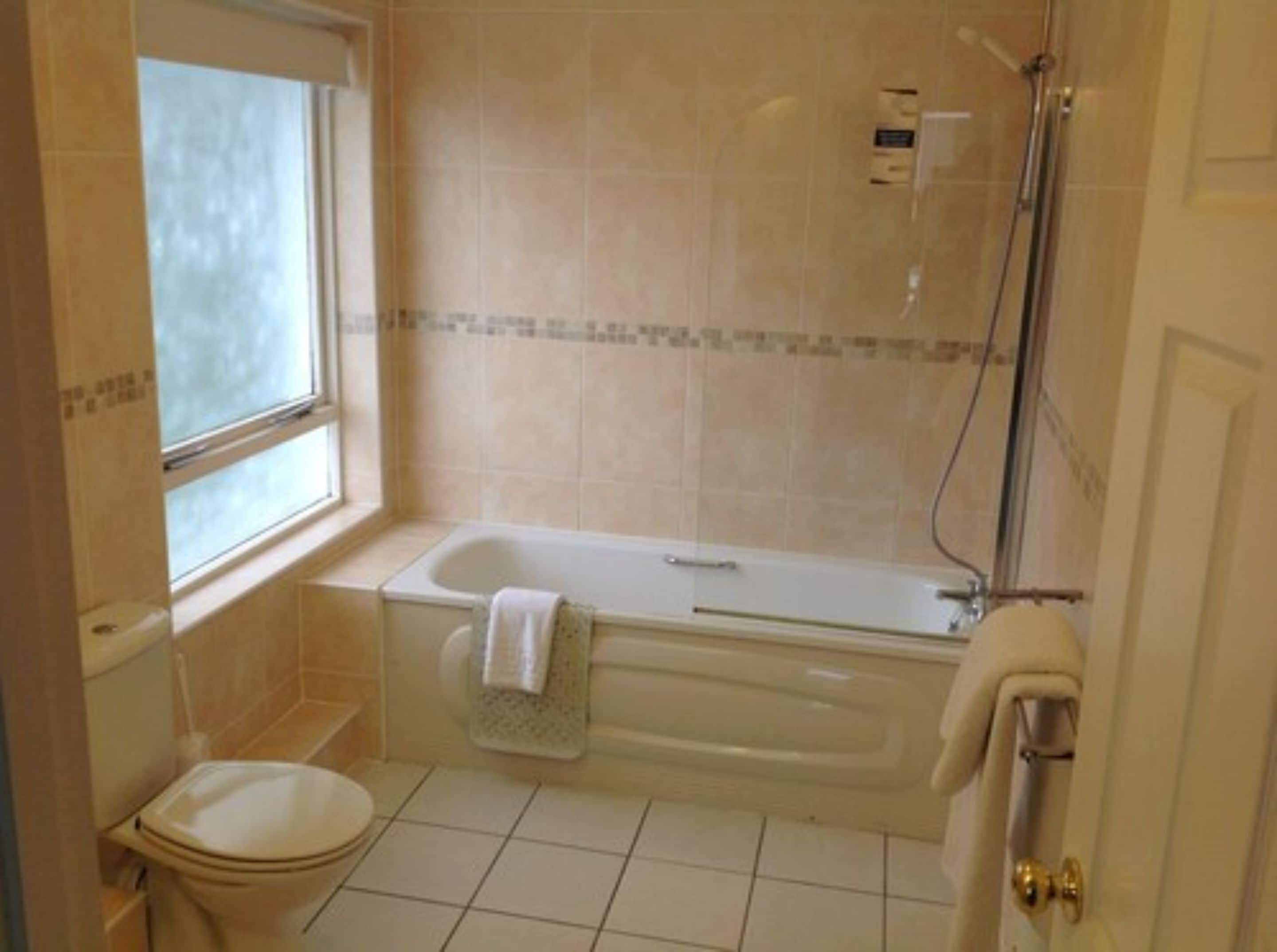 A bathroom with a bathtub, toilet, and a window.
