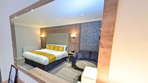 A modern hotel room with a large bed, a seating area, and a wooden accent wall. - Best Western Premier Heronston Hotel & Spa (Bridgend)