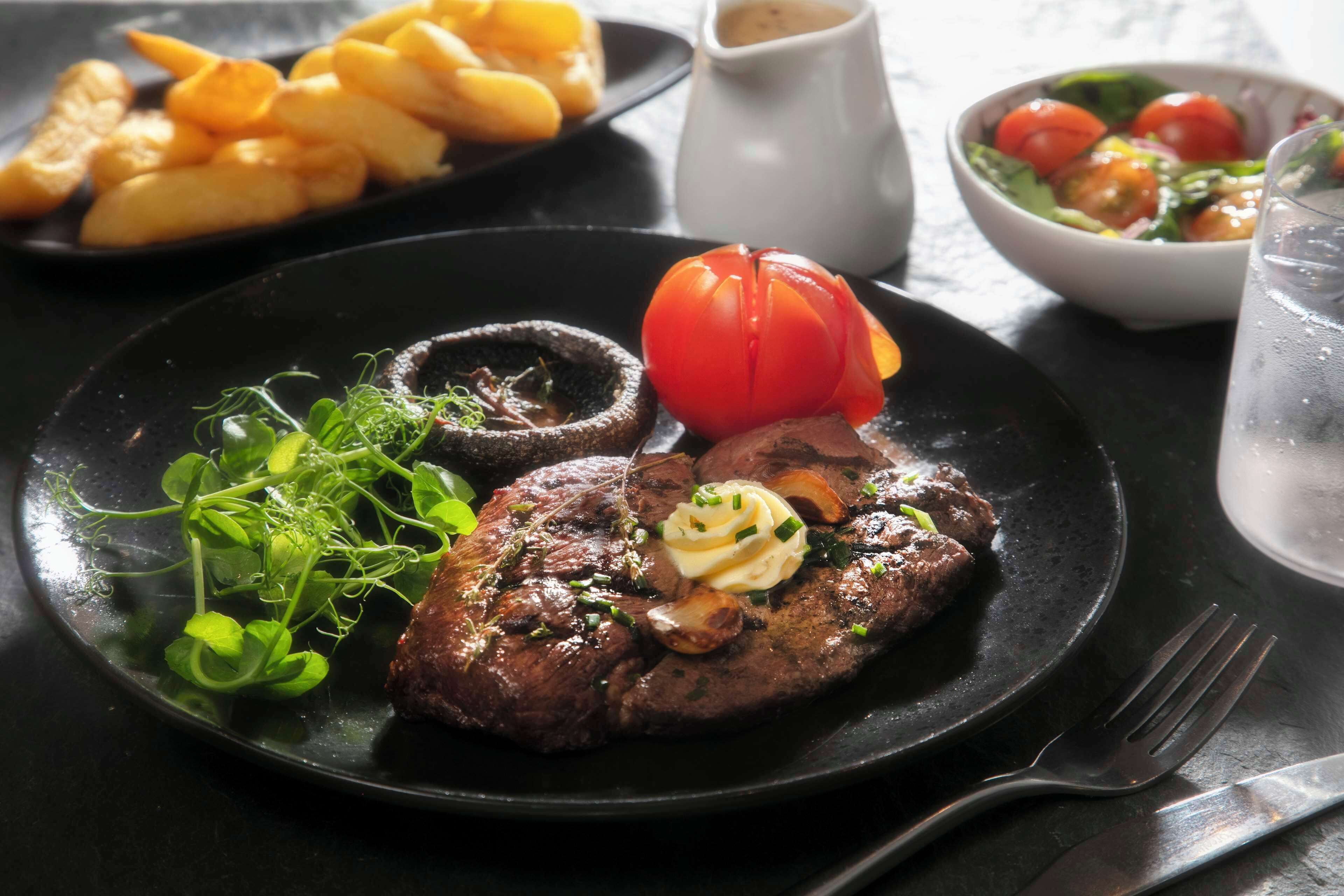 A plate with steak, mushrooms, and a tomato on a black plate.