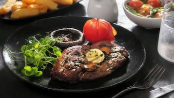 A plate with steak, mushrooms, and a tomato on a black plate.