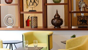 A modern interior with yellow chairs and tables, decorative vases, and a wooden shelf with various items. - Best Western Premier Heronston Hotel & Spa (Bridgend)