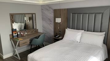 A modern hotel room with a large bed, a desk with a chair, a vanity with a mirror, and a nightstand with a lamp.