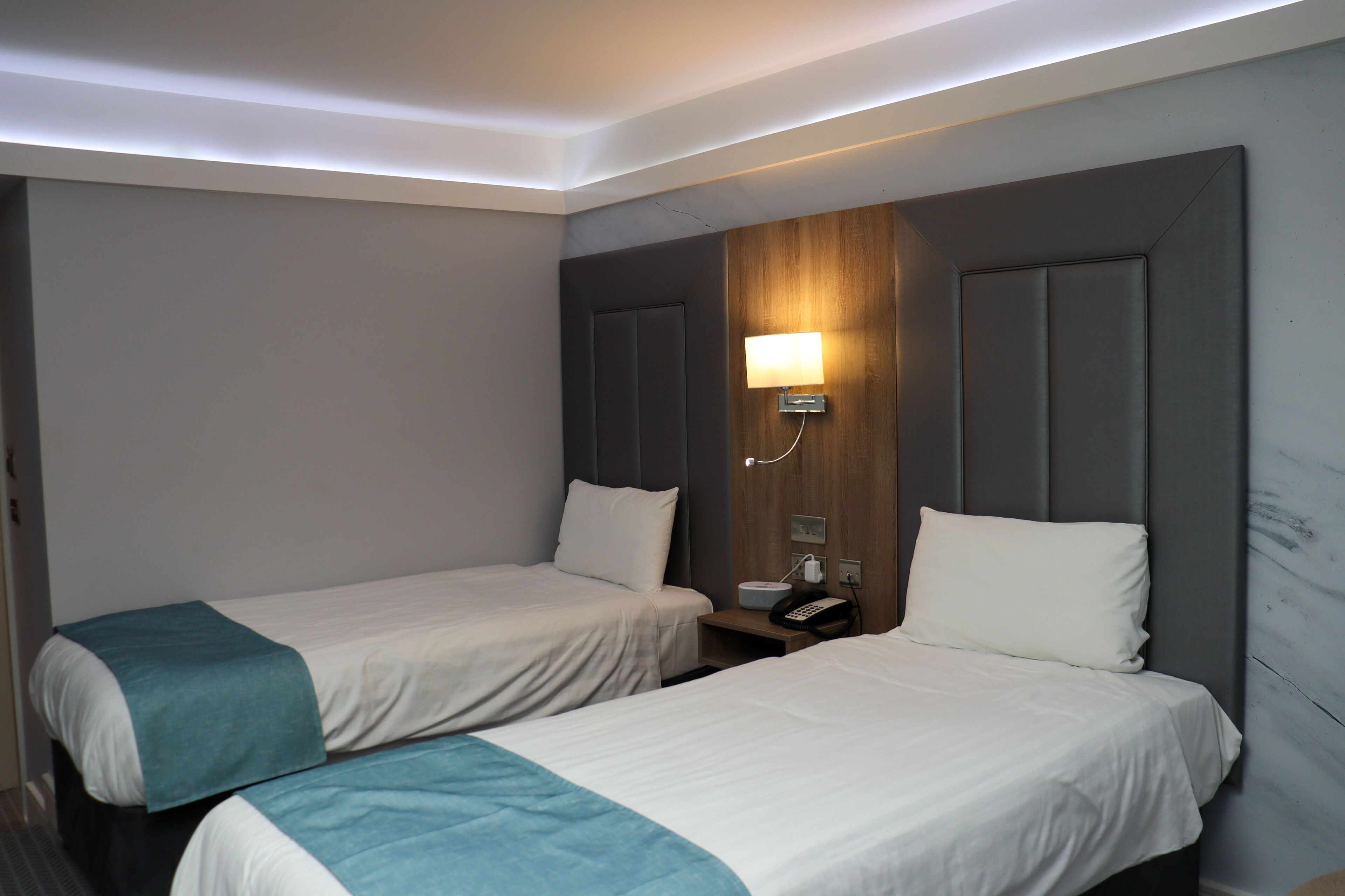 Una habitación de hotel con dos camas, una mesita de noche con lámpara y un teléfono en la pared.