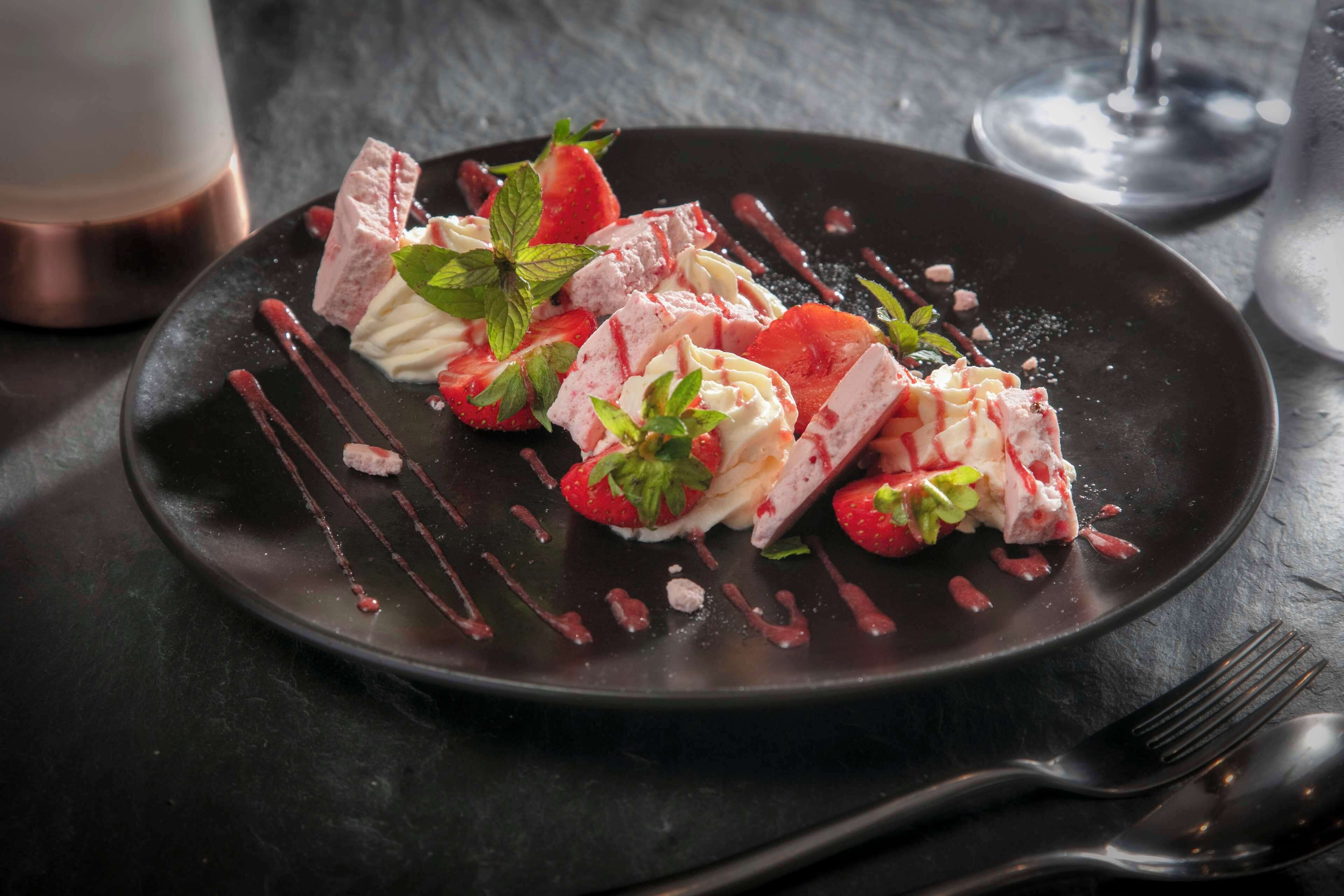A dessert plate with strawberries, mint, and chocolate on a dark plate.