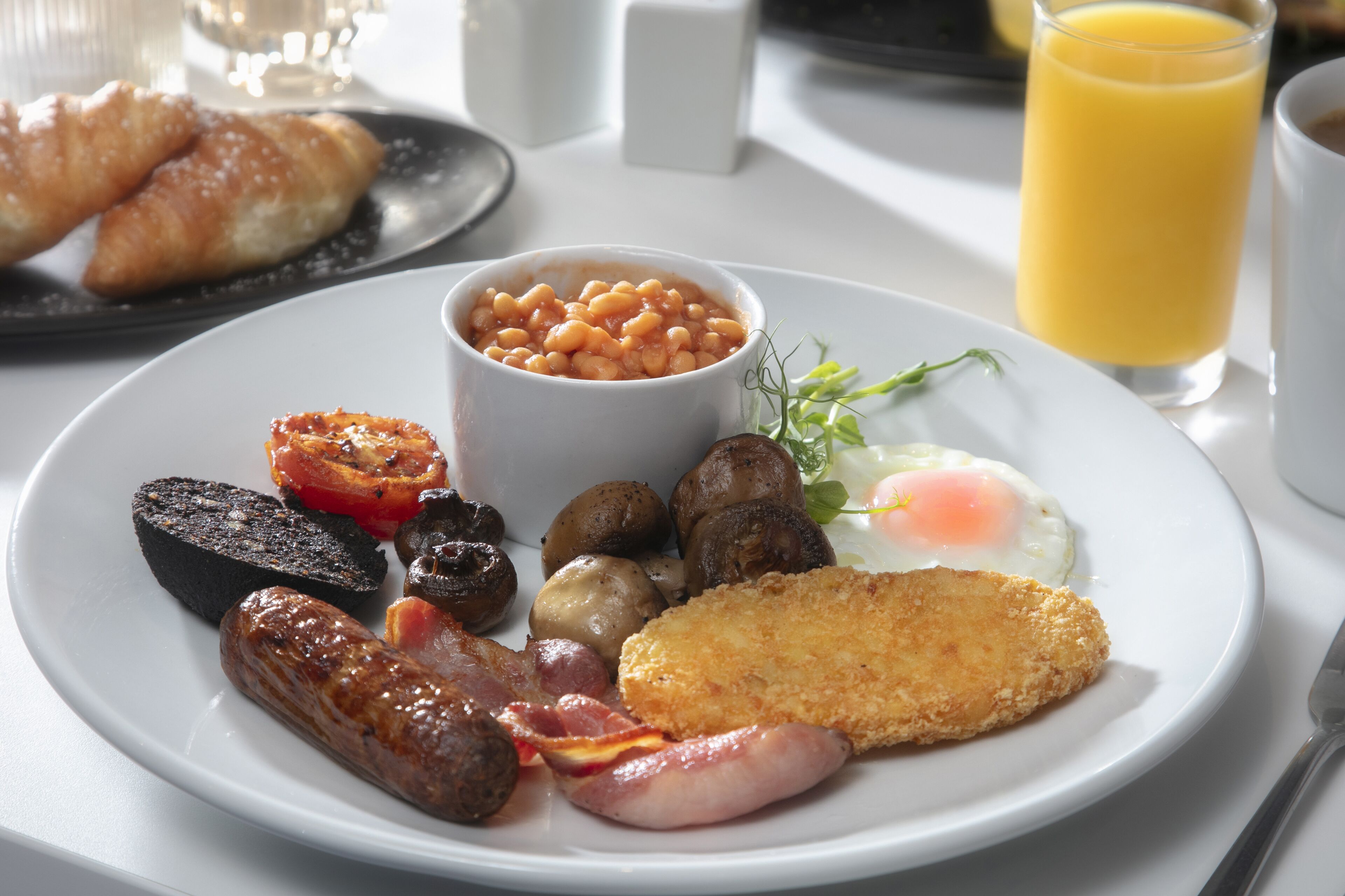 A breakfast plate with eggs, sausages, mushrooms, baked beans, and a fried cutlet.