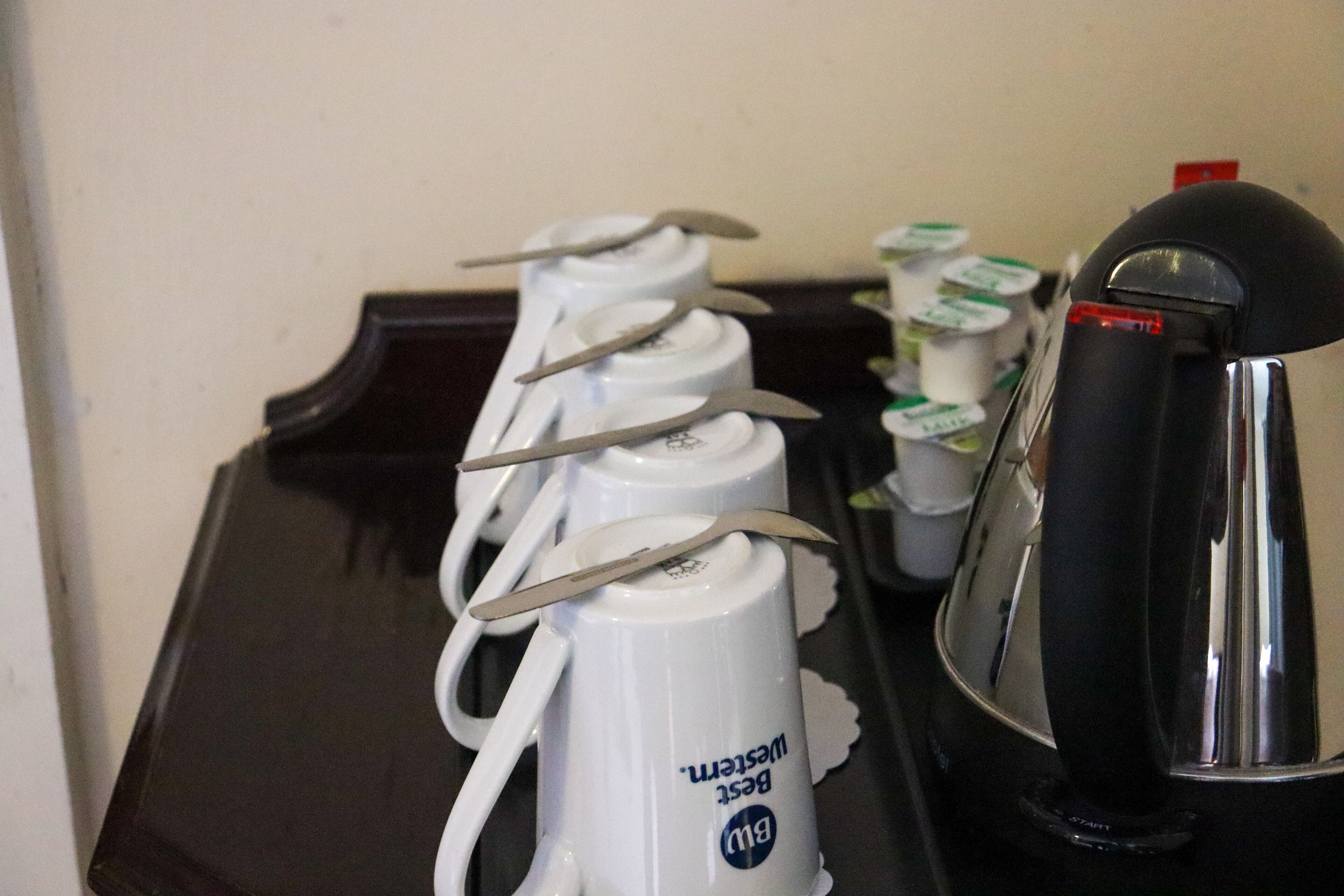 A tray with four white coffee cups, each with a spoon, and a black coffee machine.