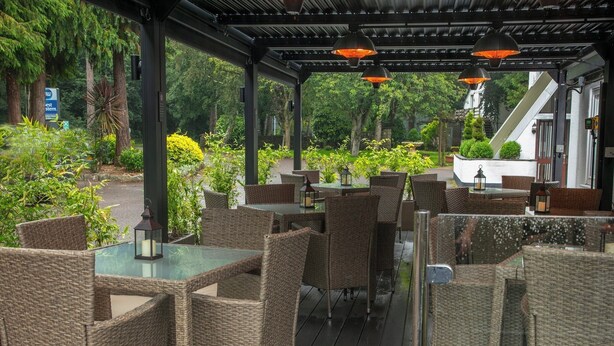 An outdoor patio with wicker furniture, tables, and hanging lanterns. - Best Western Premier Heronston Hotel & Spa (Bridgend)