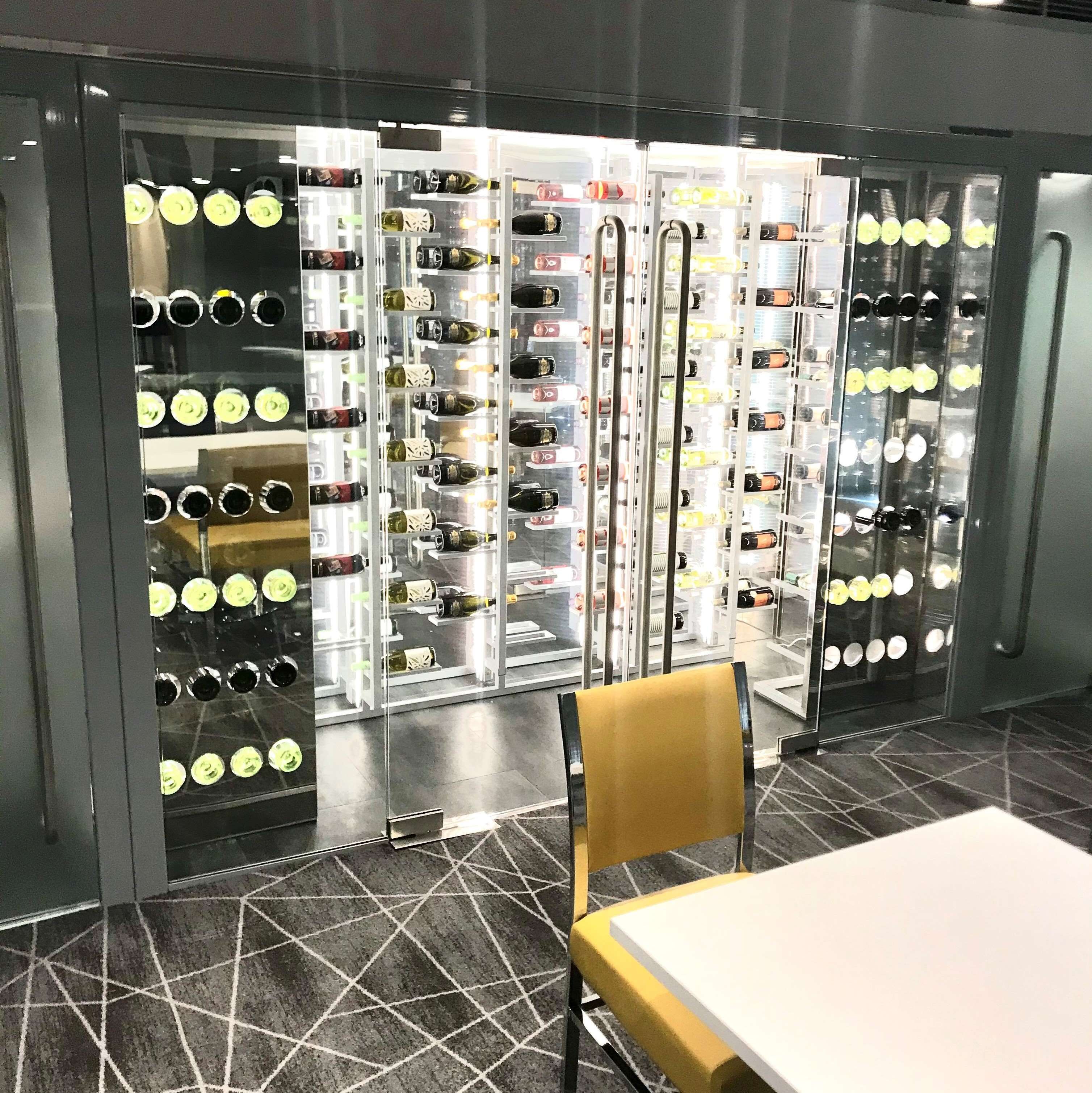 A room with a table and chairs, a patterned floor, and a wall with multiple wine bottle displays.