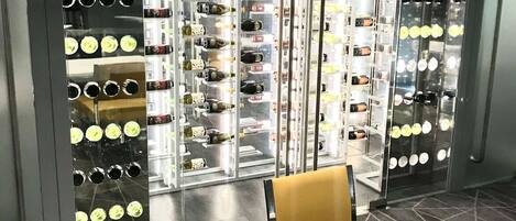 A room with a table and chairs, a patterned floor, and a wall with multiple wine bottle displays.