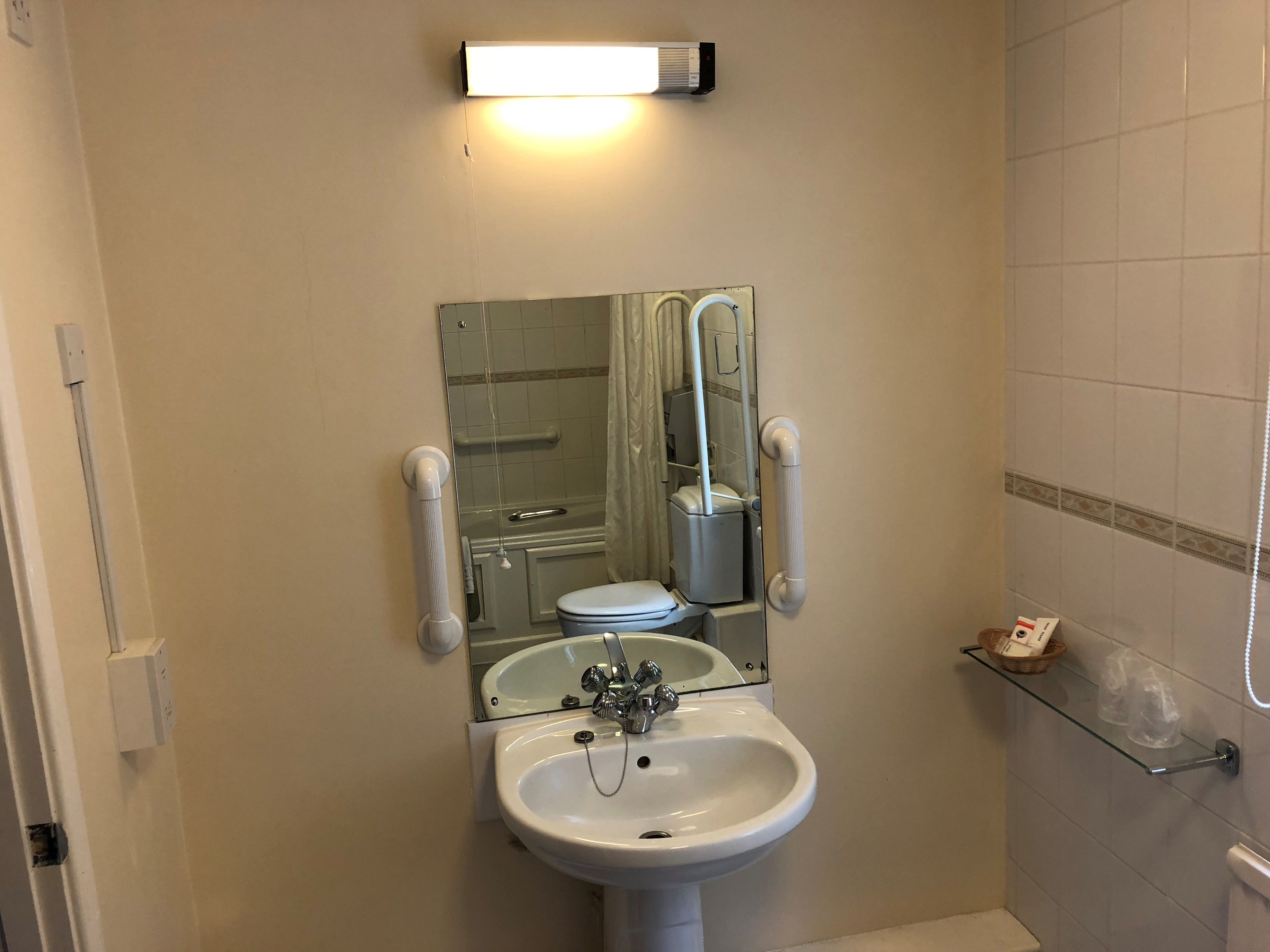 Ein Badezimmer mit weißem Waschbecken, einem Spiegel, einer Toilette und einer Dusche.