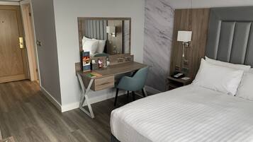 Ein Hotelzimmer mit einem Bett, einem Schreibtisch mit Stuhl, einem Nachttisch, einem Spiegel und einer Marmorwand.