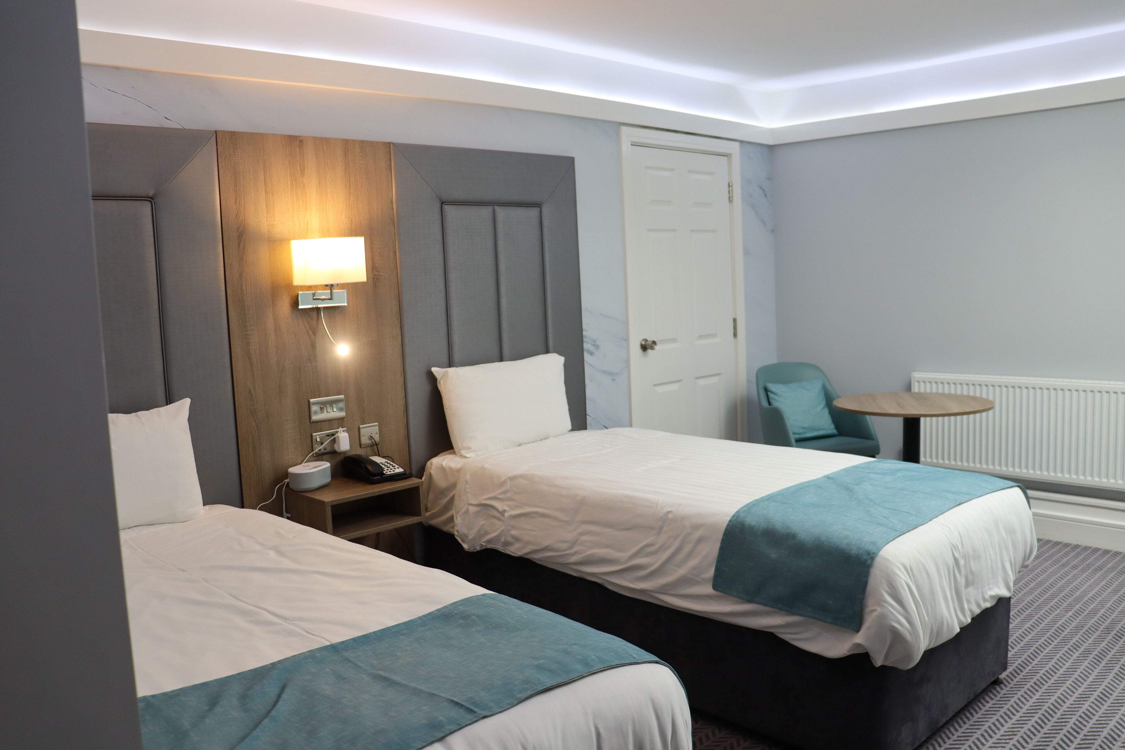 Une chambre d’hôtel avec deux lits, une table de chevet avec une lampe, une chaise et une petite table ronde.