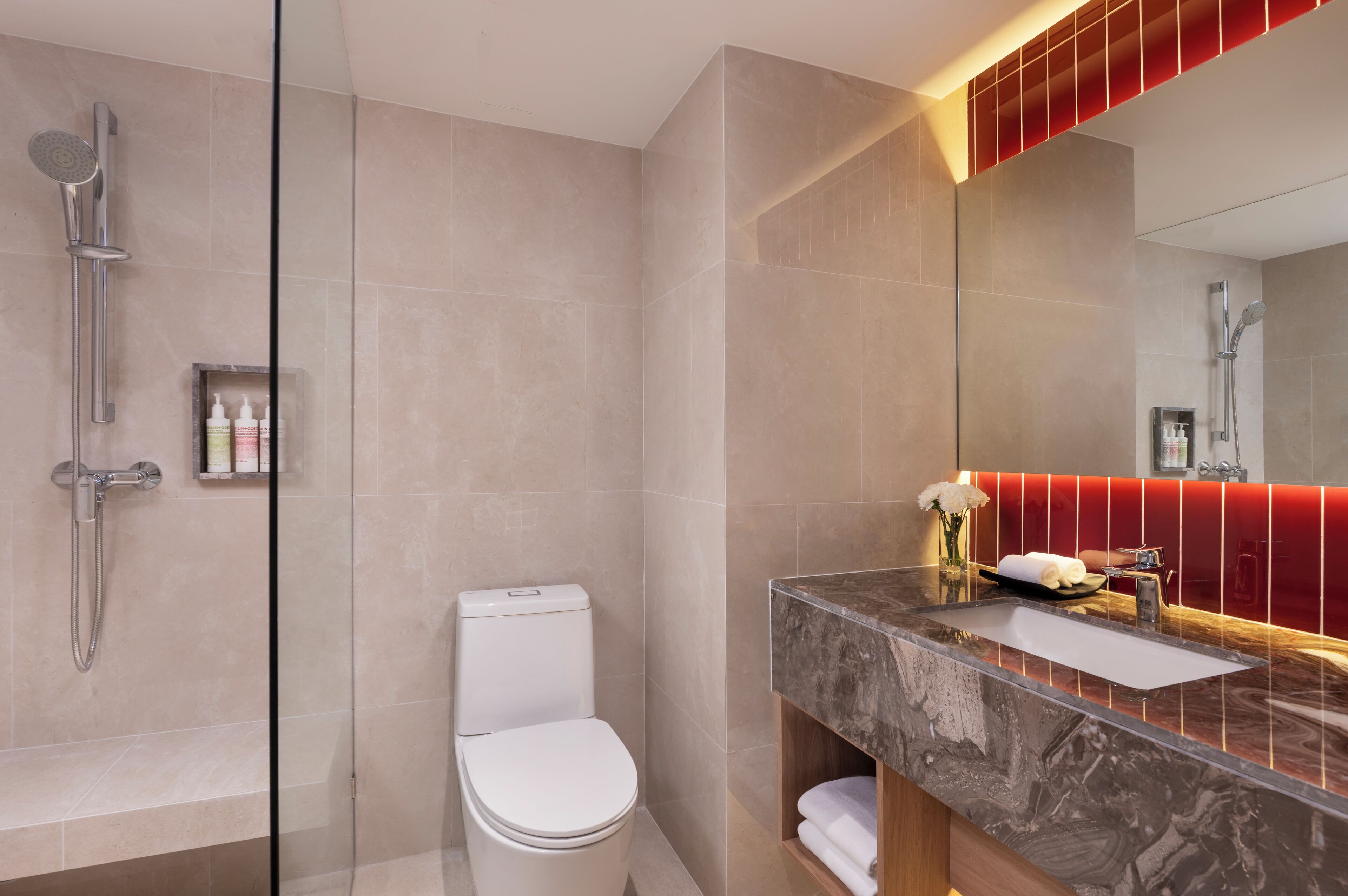 A modern bathroom with a glass-enclosed shower, a white toilet, and a marble vanity with a red-lit mirror.