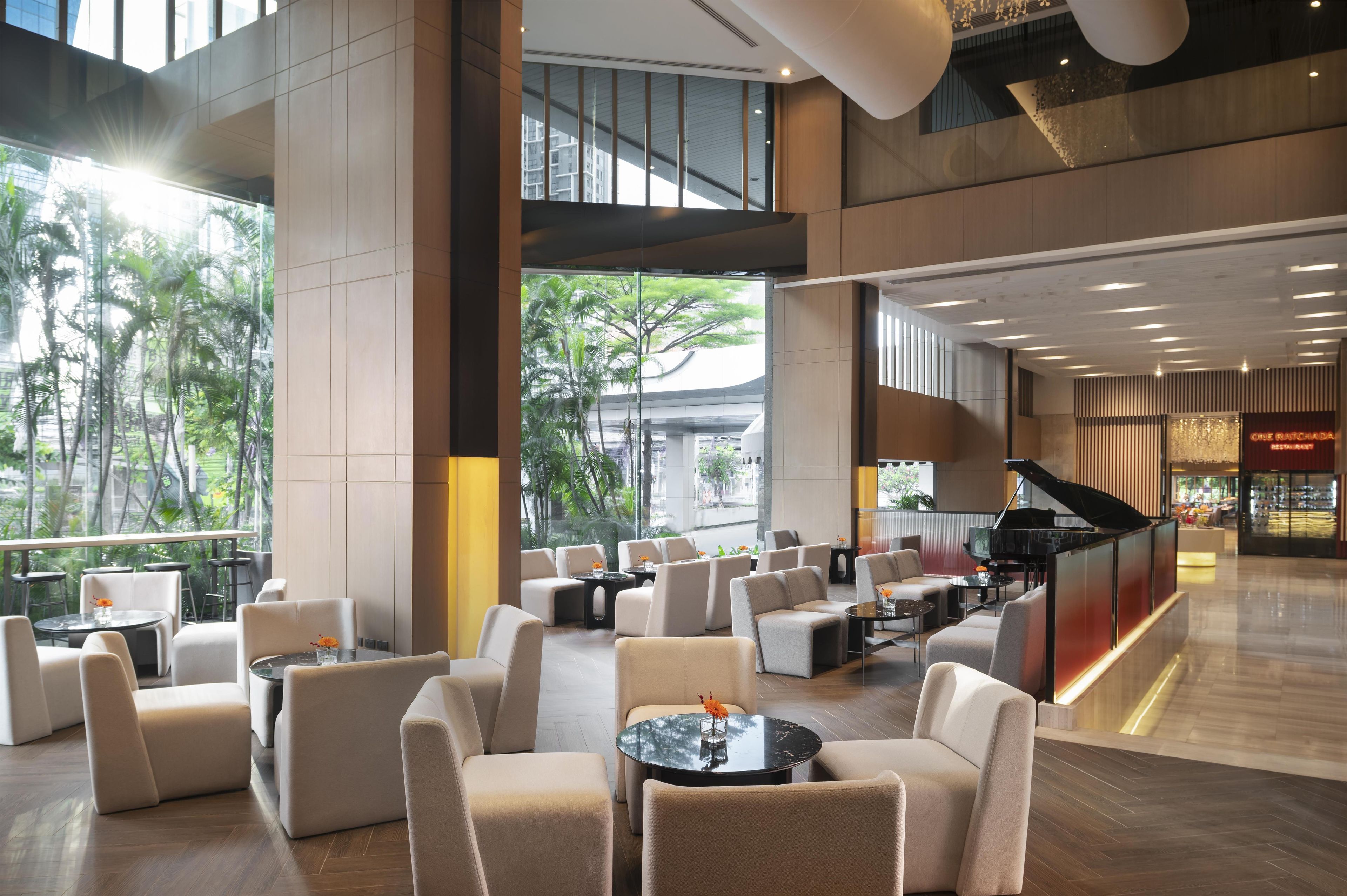 A spacious lobby with multiple seating areas, a grand piano, and a view of palm trees through large windows.
