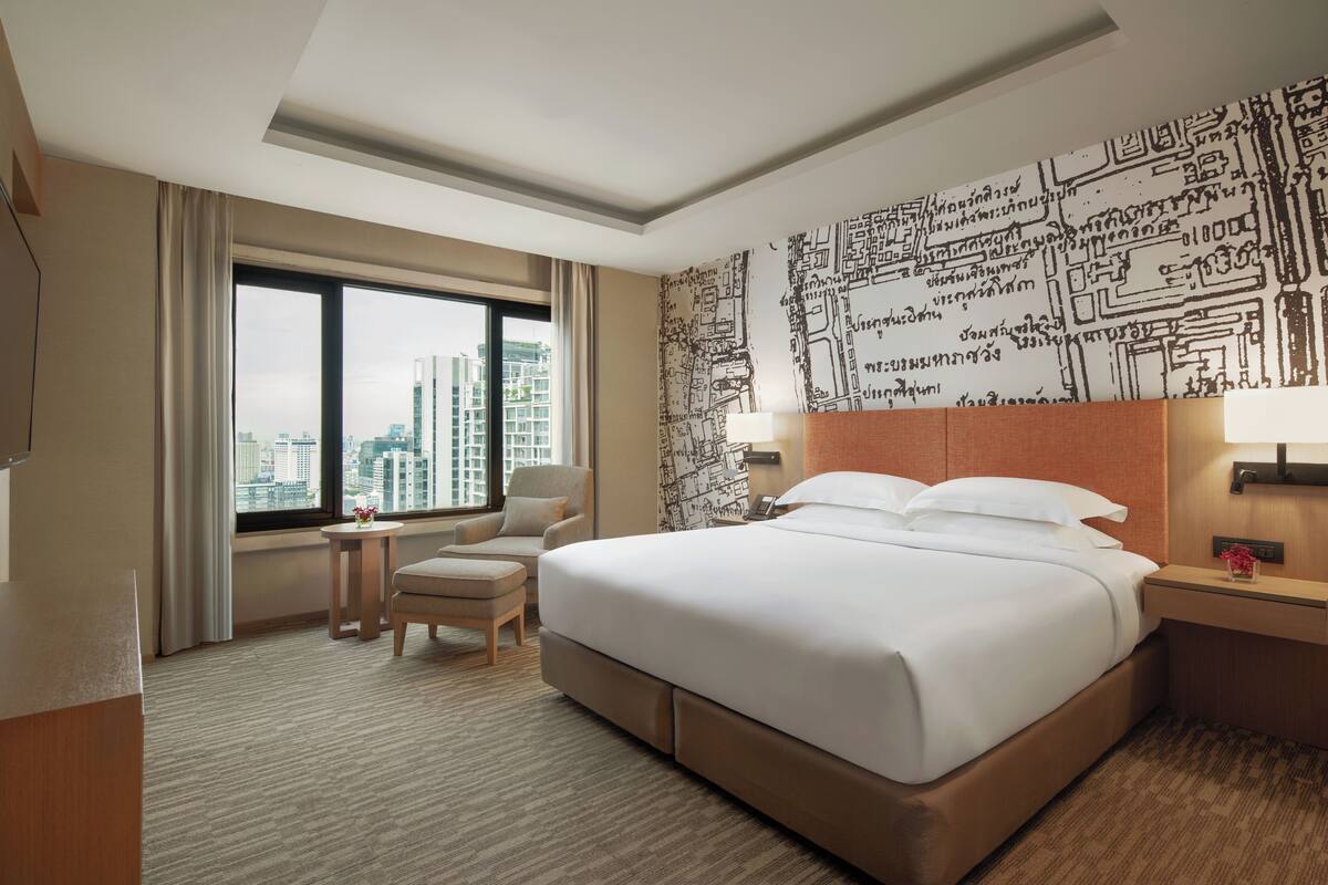 A hotel room with a large bed, a desk, a chair, and a view of the cityscape.