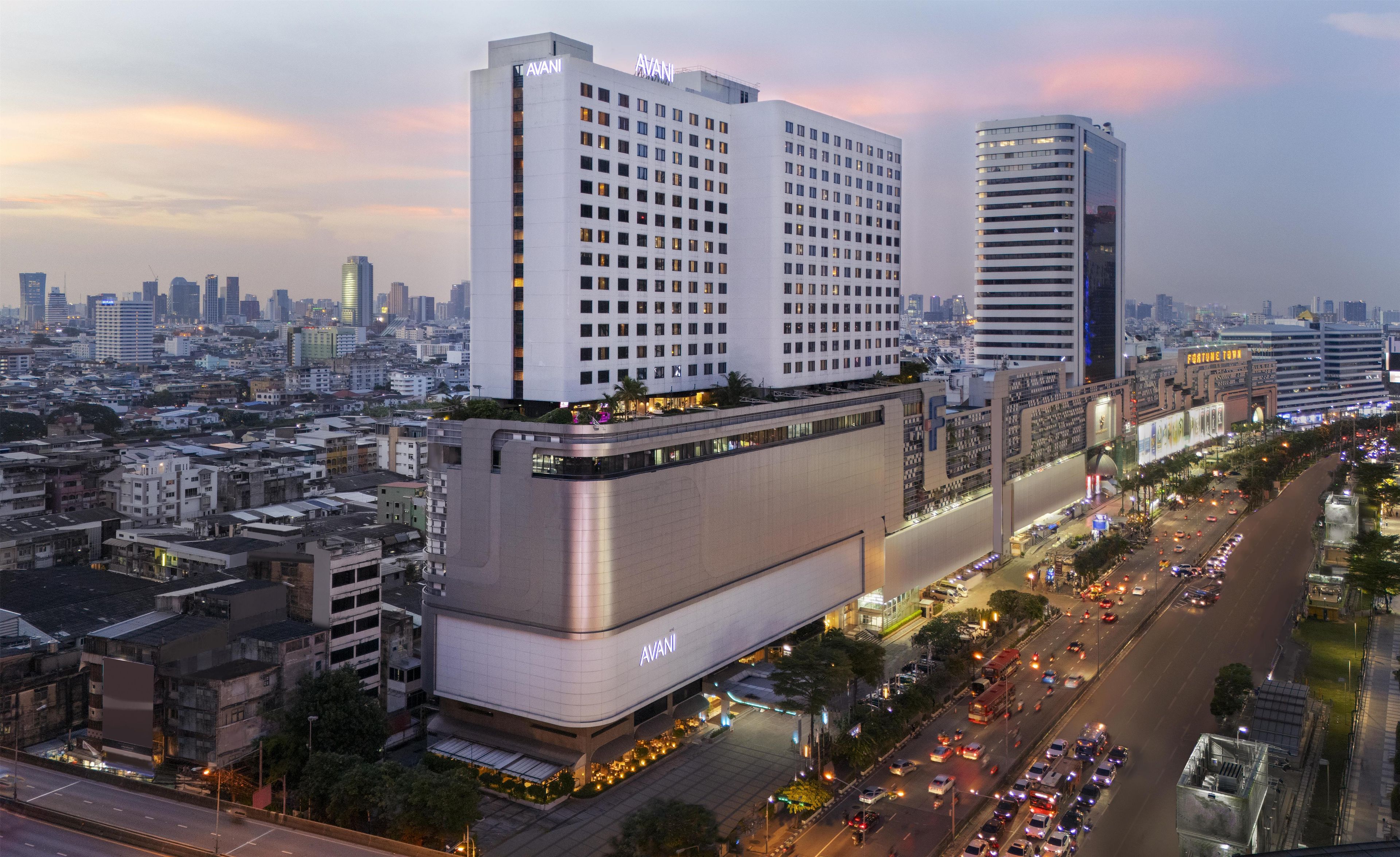 A high-rise hotel with multiple floors, a prominent 'AVANI' sign, and a busy urban street below.