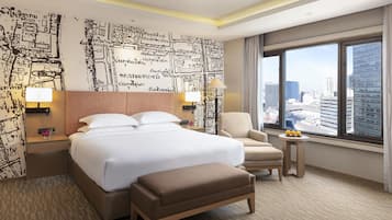 A hotel room with a large bed, a sitting area with a chair and a small table, a view of the cityscape through a large window, and a wall with a map design.
