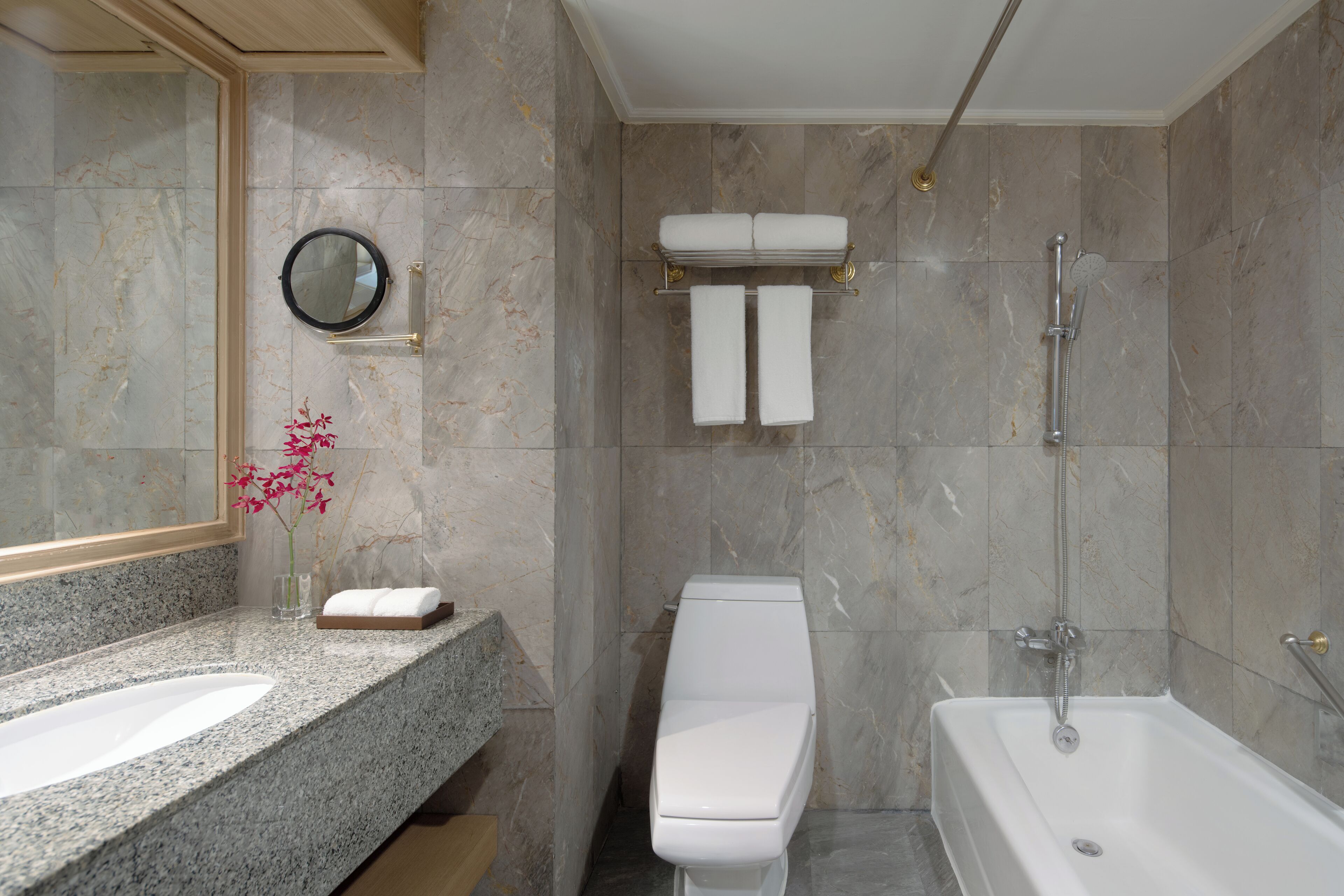 A modern bathroom with a granite countertop, a toilet, a bathtub, and a shower.