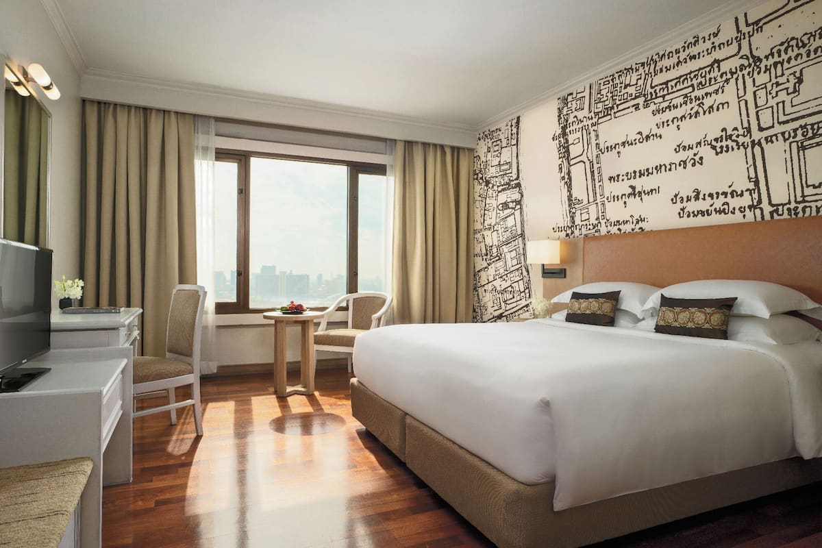 A hotel room with a bed, a desk, a chair, a small table, and a window with curtains.