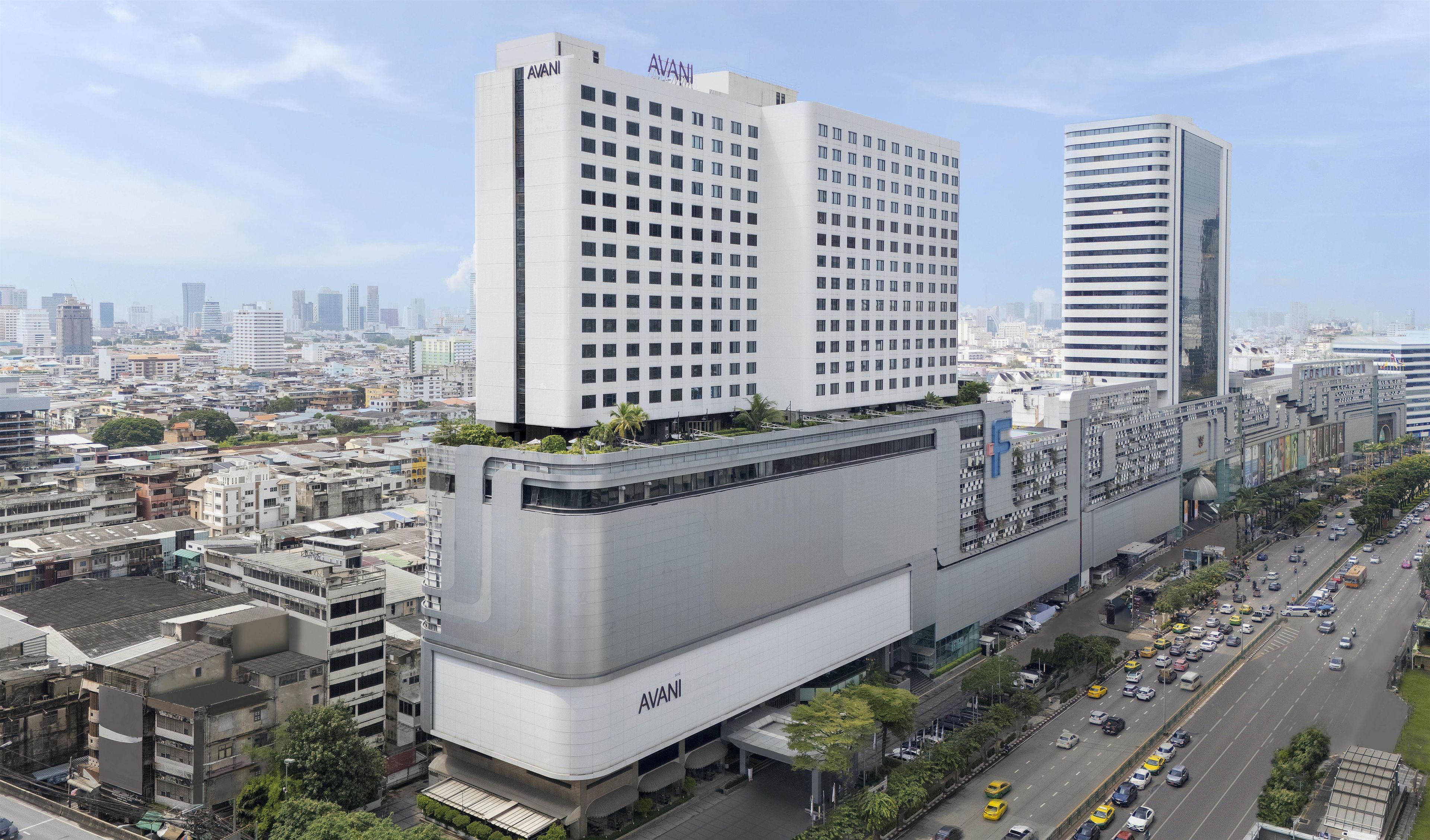A modern hotel with a prominent 'AVANI' sign, surrounded by urban buildings and a busy street.