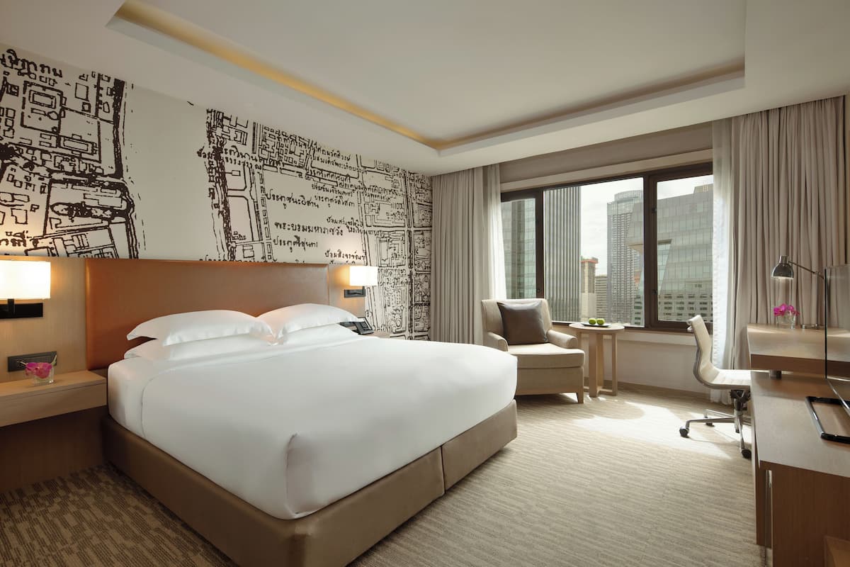A hotel room with a large bed, a desk, a chair, a nightstand, and a window with a city view.