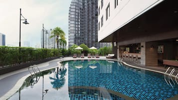 A swimming pool with a tiled design, surrounded by lounge chairs and umbrellas, with high-rise buildings in the background.