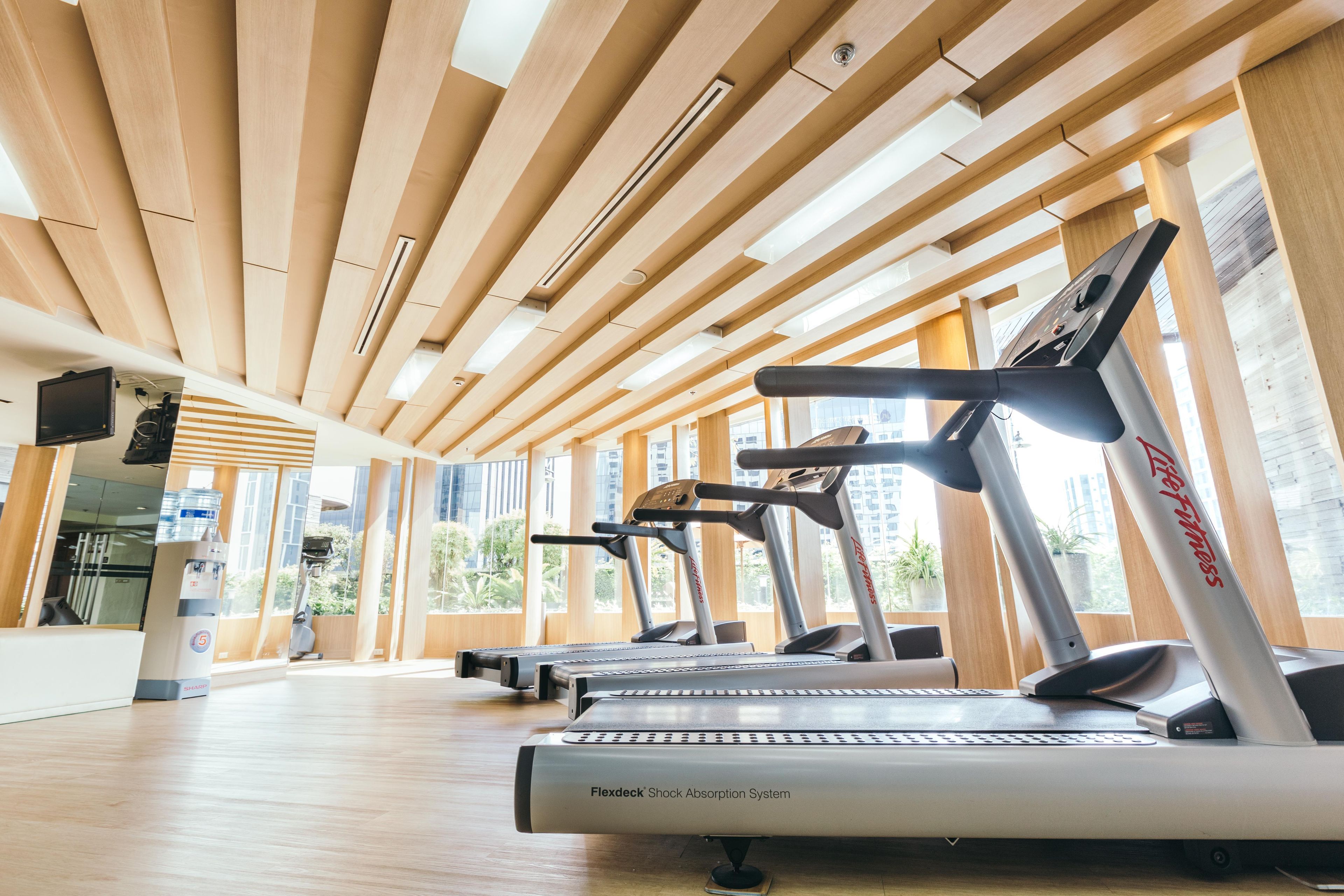 A gym with multiple treadmills, wooden ceiling, and large windows.