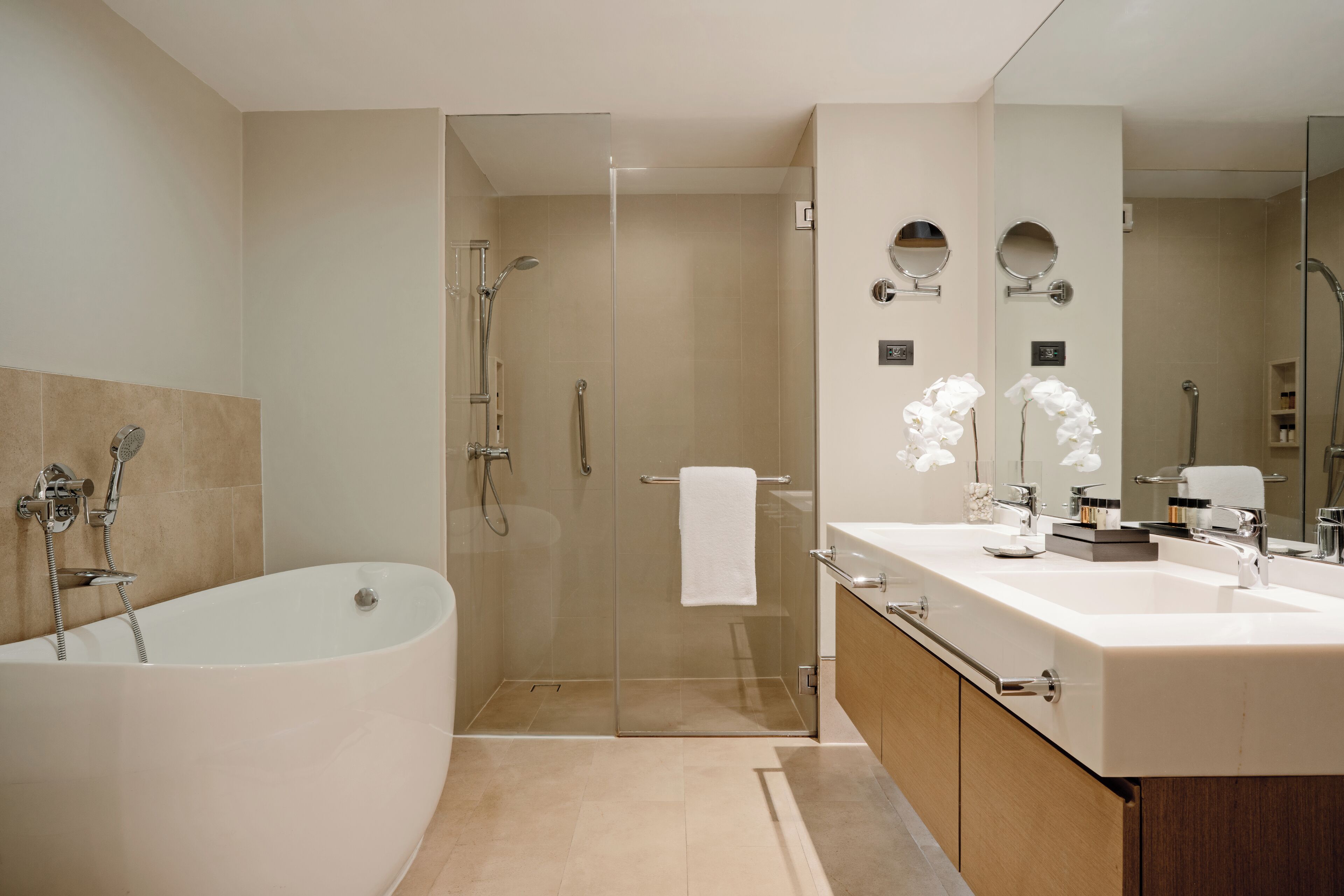 A modern bathroom with a freestanding bathtub, a glass-enclosed shower, and a vanity with a double sink and mirrors.