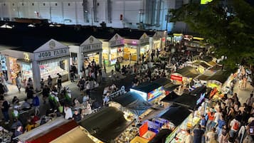 Um mercado ao ar livre movimentado com diversos quiosques e lojas, incluindo Jodd Fairs, sob um céu noturno.